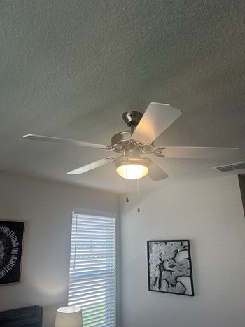 A ceiling fan with a light on in a room with two pictures on the wall.